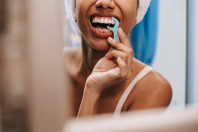 A woman is brushing her teeth in the mirror.